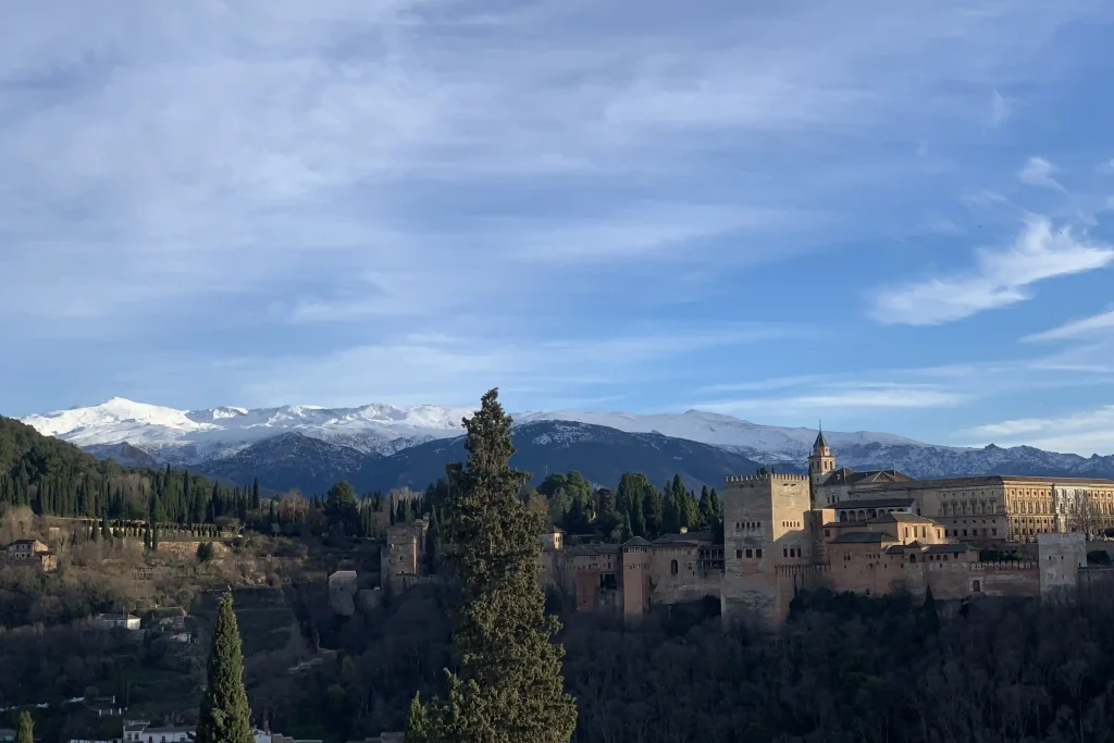 Vista dell’Alhambra di Granada con la Sierra Nevada innevata sullo sfondo e cielo azzurro in Andalusia