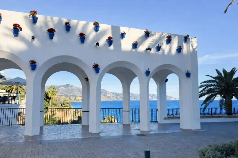 Archi bianchi del Balcón de Europa a Nerja con vasi blu, fiori rossi e vista sul mare Mediterraneo