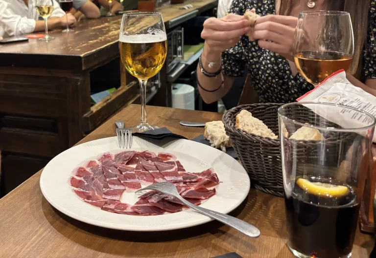 Mangiare a a Málaga Jamón ibérico servito da El Pimpi con birra e pane su tavolo di legno