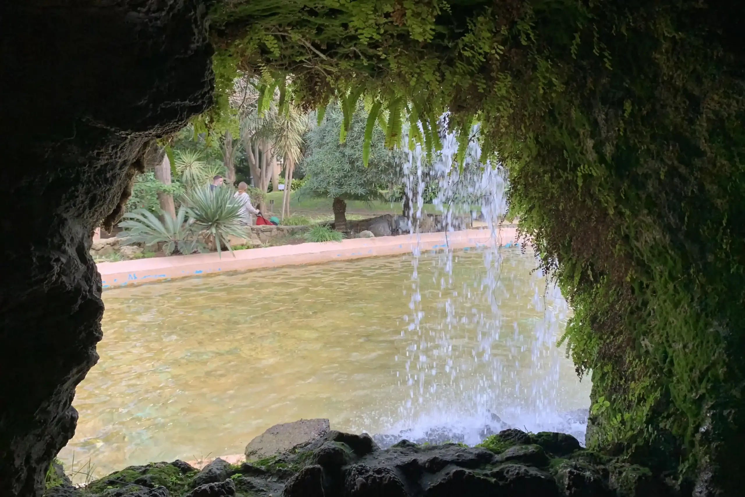 Cascata nel Parque Genovés a Cádiz vista dall’interno di una grotta con felci e vegetazione tropicale