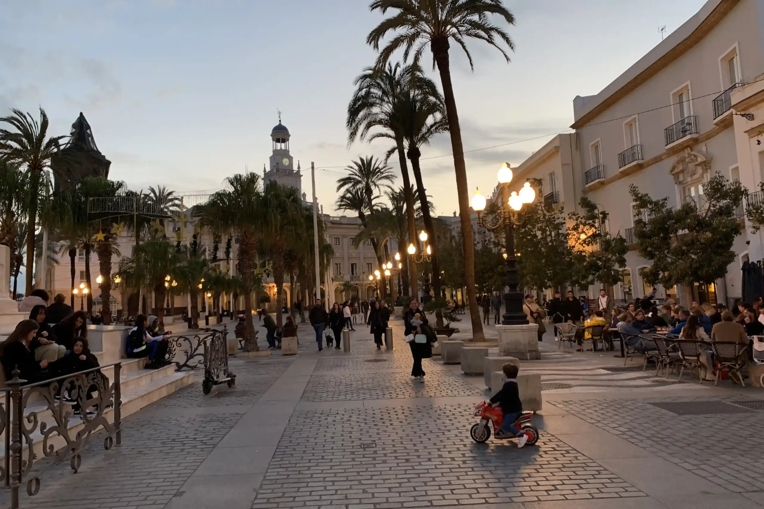 Plaza de San Juan de Dios a Cádiz al tramonto con palme, lampioni accesi e gente che passeggia