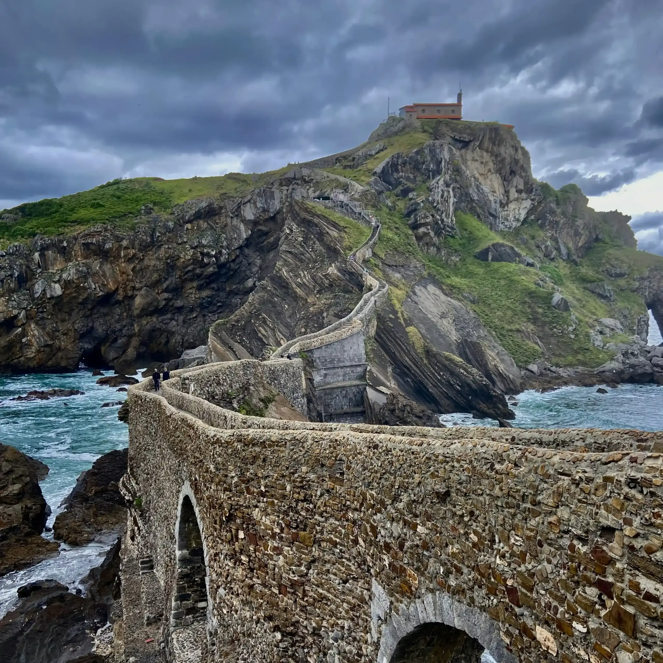 Ponte in pietra e scalinata di San Juan de Gaztelugatxe nei Paesi Baschi con oceano e cielo nuvoloso