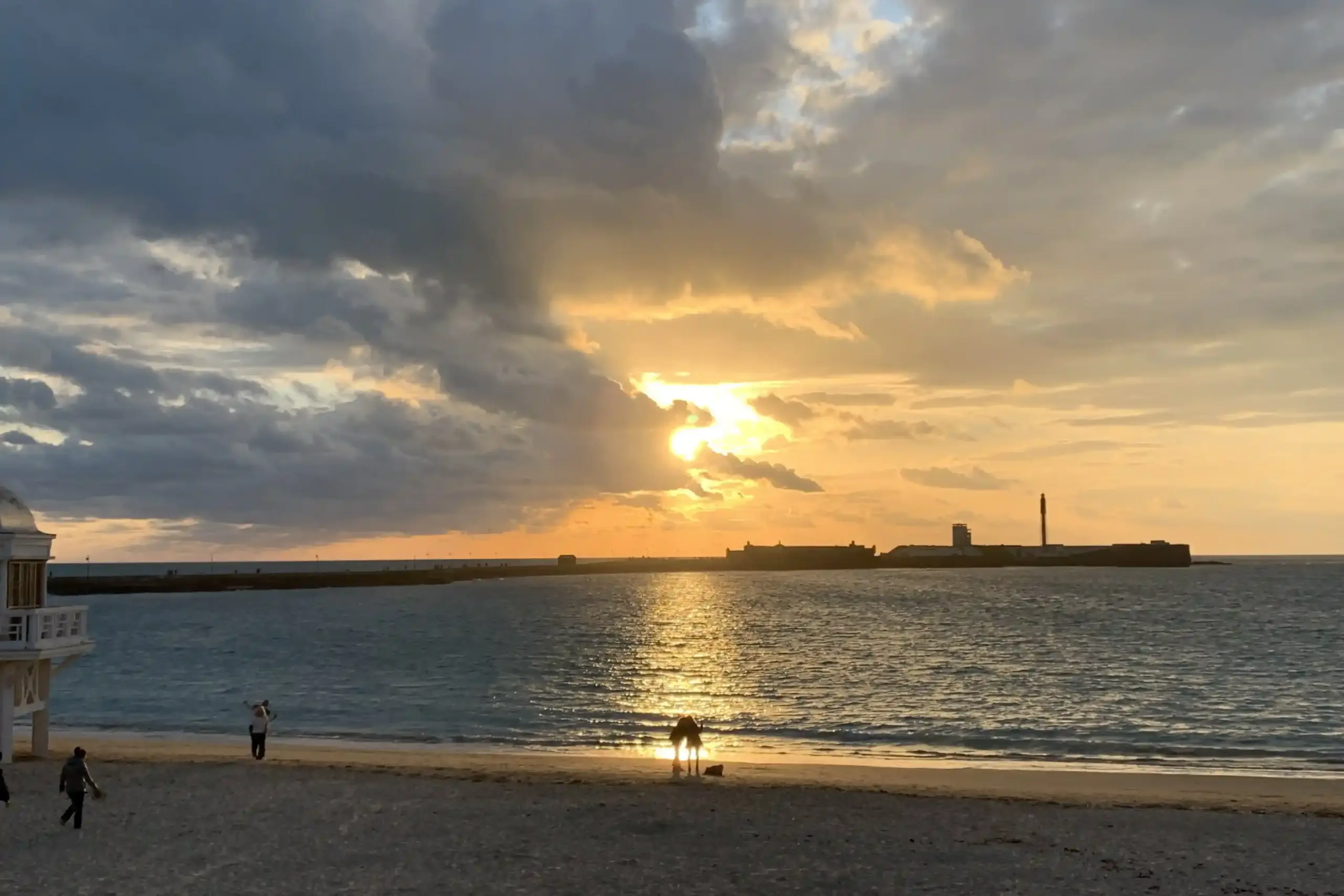 Tramonto su Playa de la Caleta a Cádiz con il Castillo de San Sebastián in silhouette e riflessi dorati sull’oceano