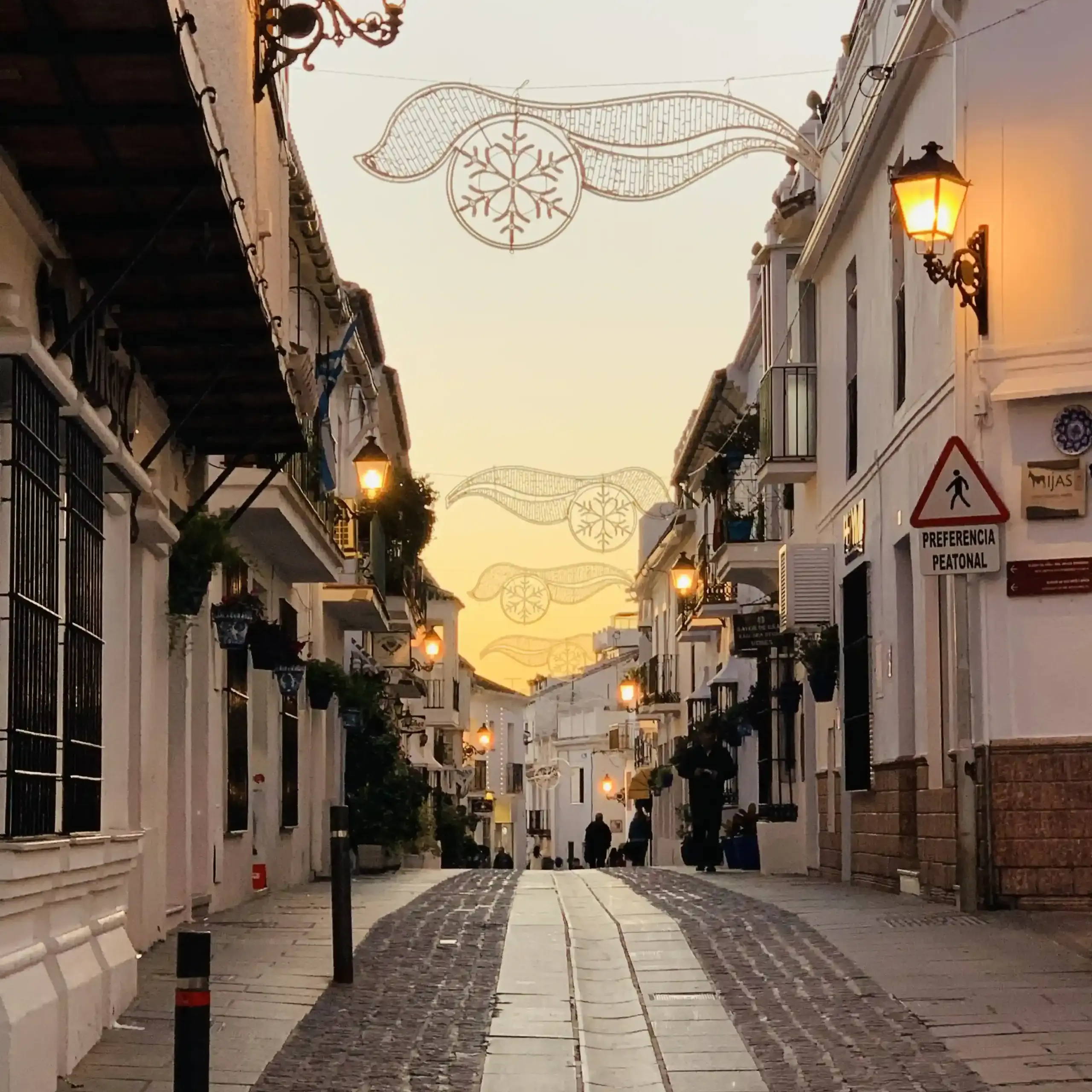 Calle Málaga a Mijas Pueblo al tramonto con case bianche, lampioni accesi e strada acciottolata