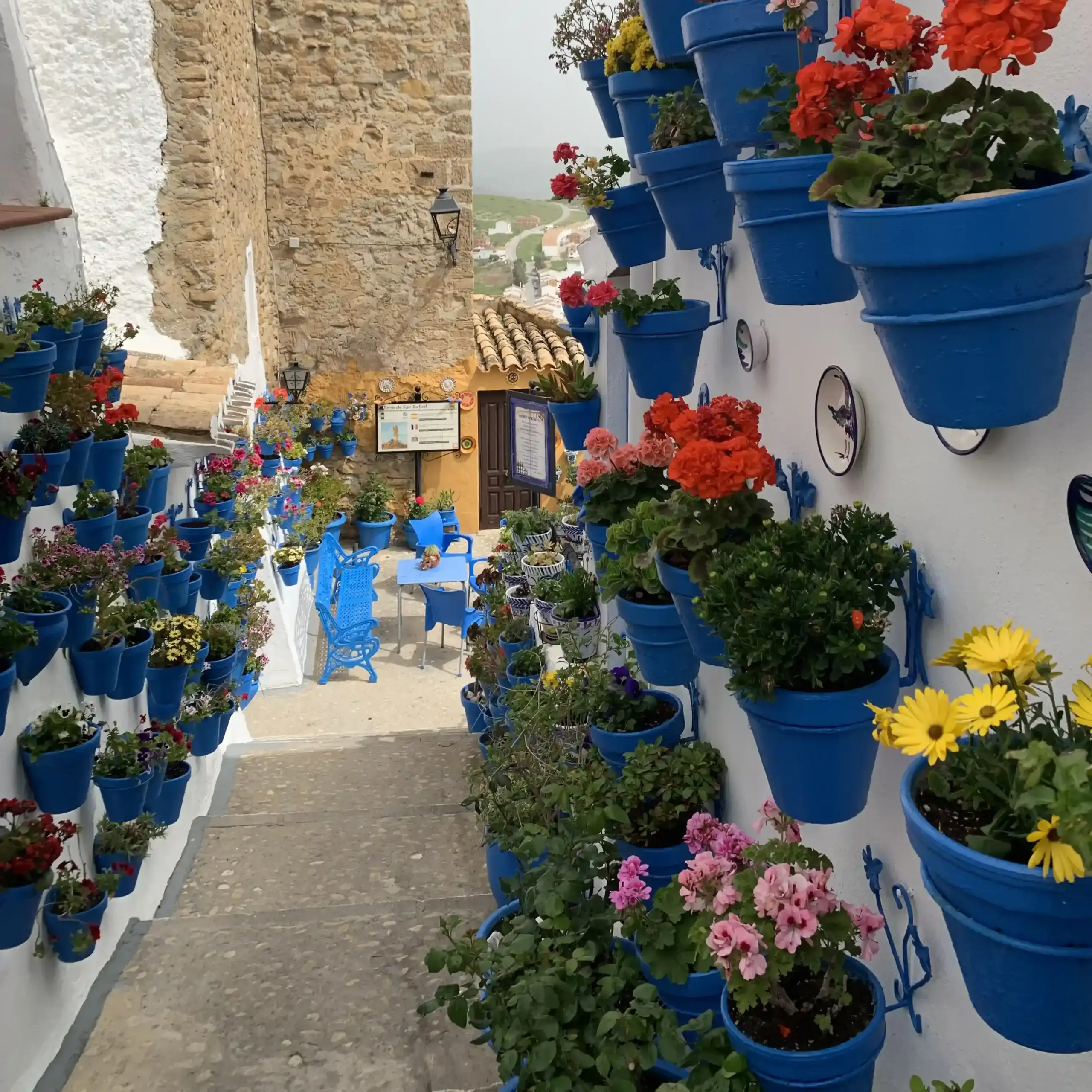 Scalinata fiorita di Iznájar con vasi blu, fiori colorati e castello sullo sfondo
